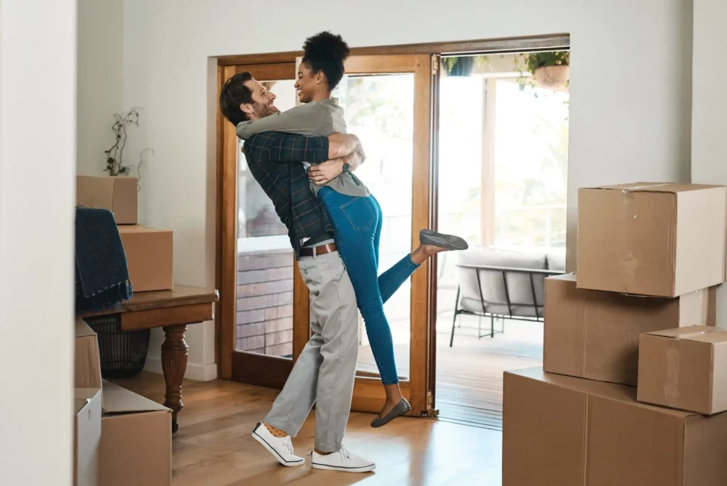 happy couple celebrating new home with husband lifting his wife excited romantic love celebration together smiling loving carefree man woman modern real estate property scaled